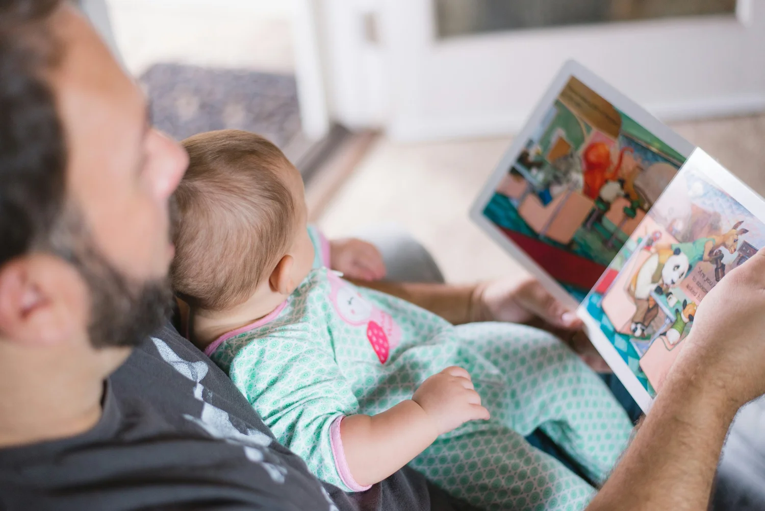 A man holding an infant while reading a colourful bilingual children's book